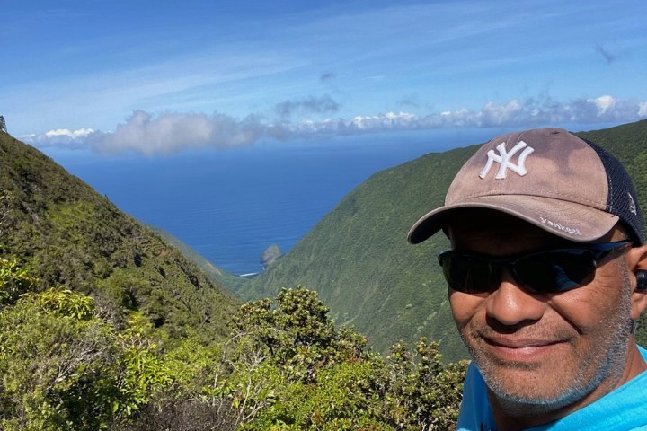 a man wearing a hat and sunglasses with a mountain in the background